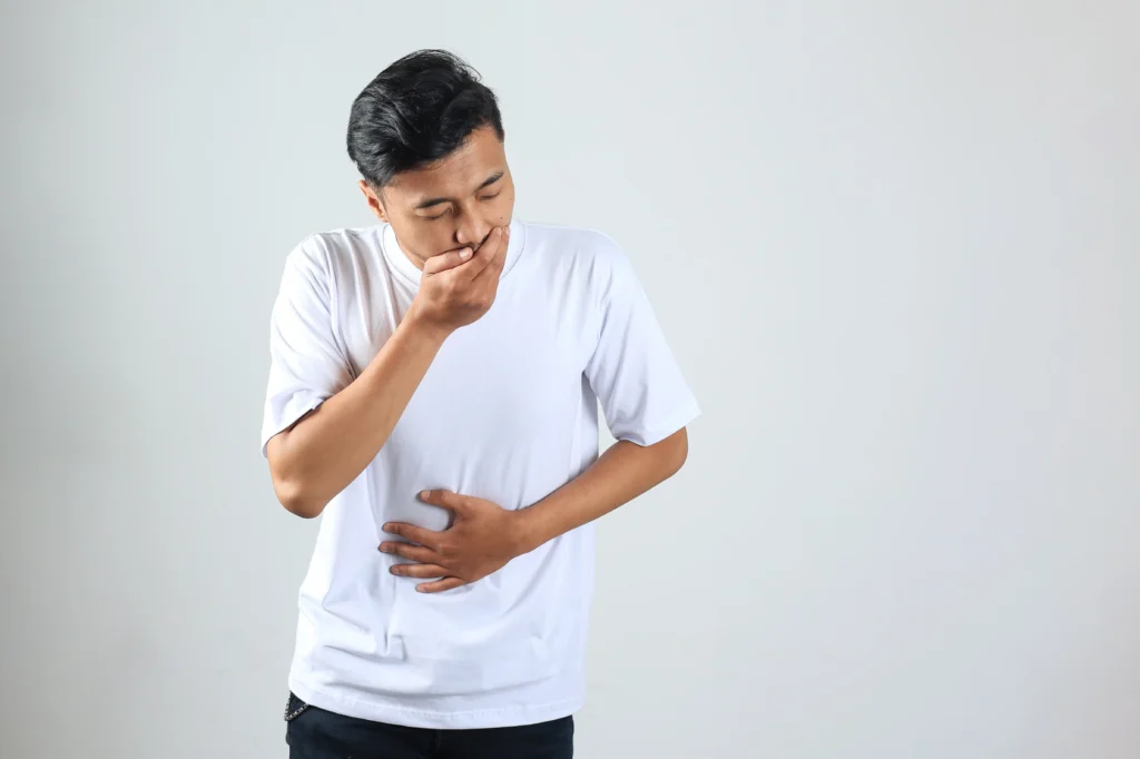 A man holding his stomach and covering his mouth, showing signs of nausea or stomach pain, which are common symptoms of H. pylori