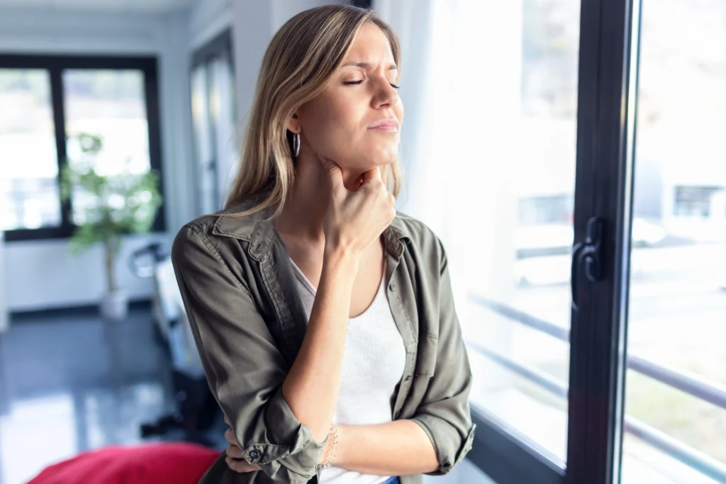 A woman holding her throat in discomfort, showing signs of dysphagia