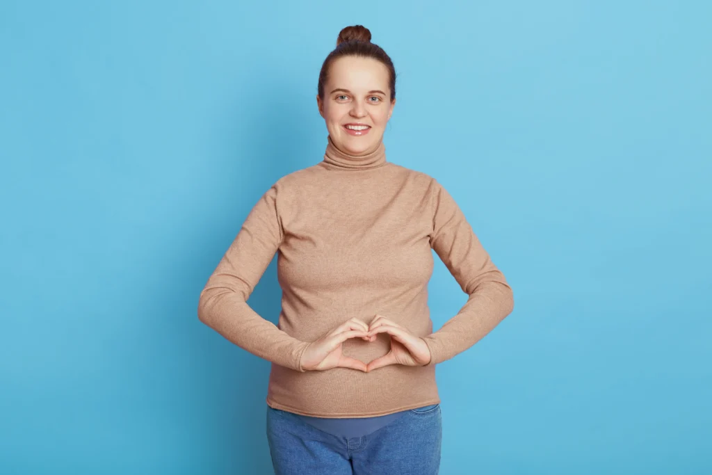 A smiling woman forms a heart shape with her hands over her stomach, symbolizing good digestive system health.