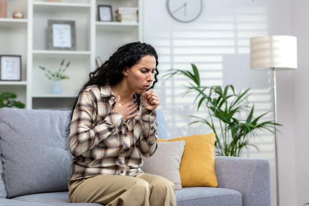 A woman clutching her chest and coughing while experiencing heartburn - a common symptom of acid reflux.