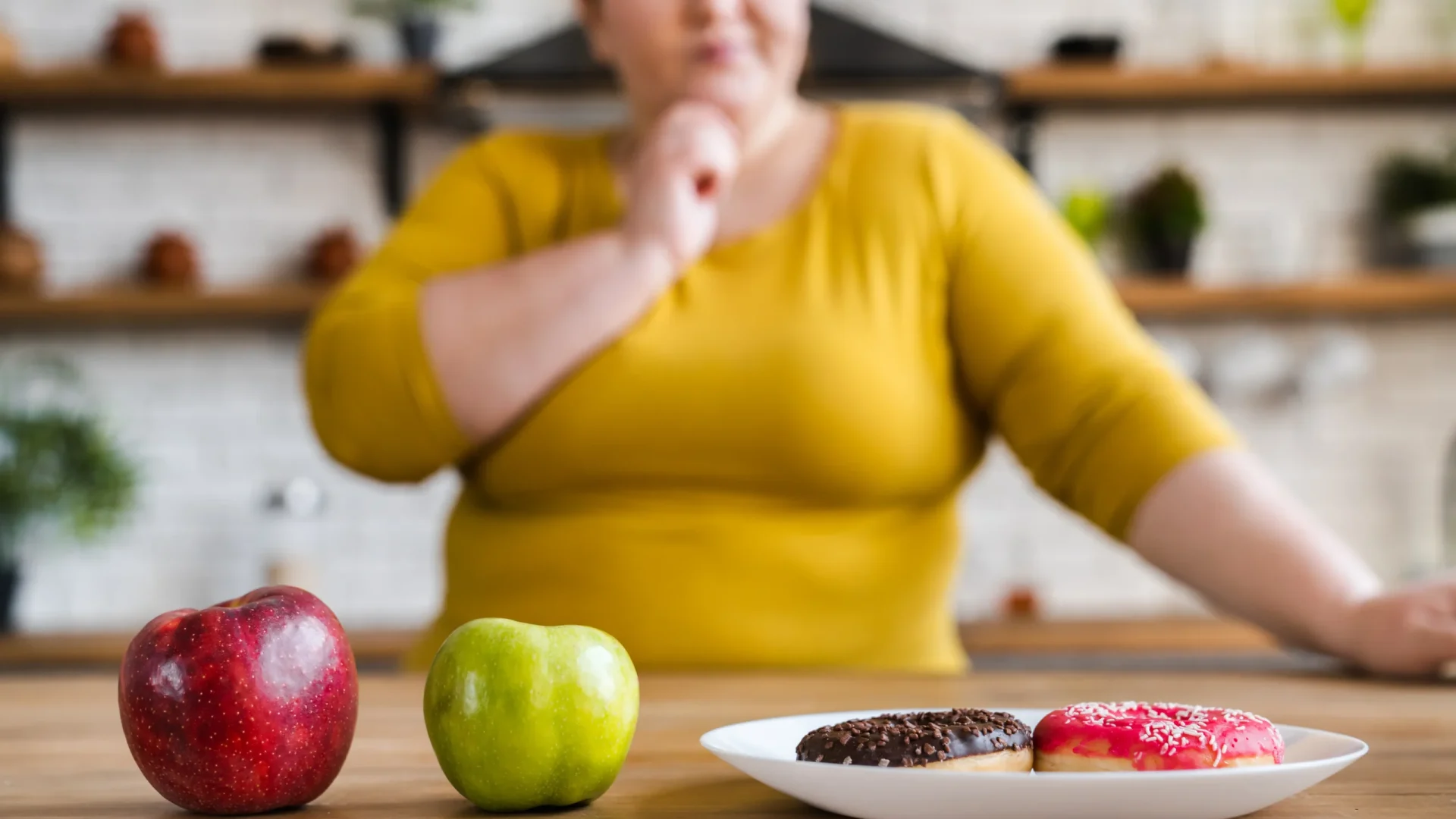A woman feels bloated after eating healthy, with a plate of food and apples on the table.